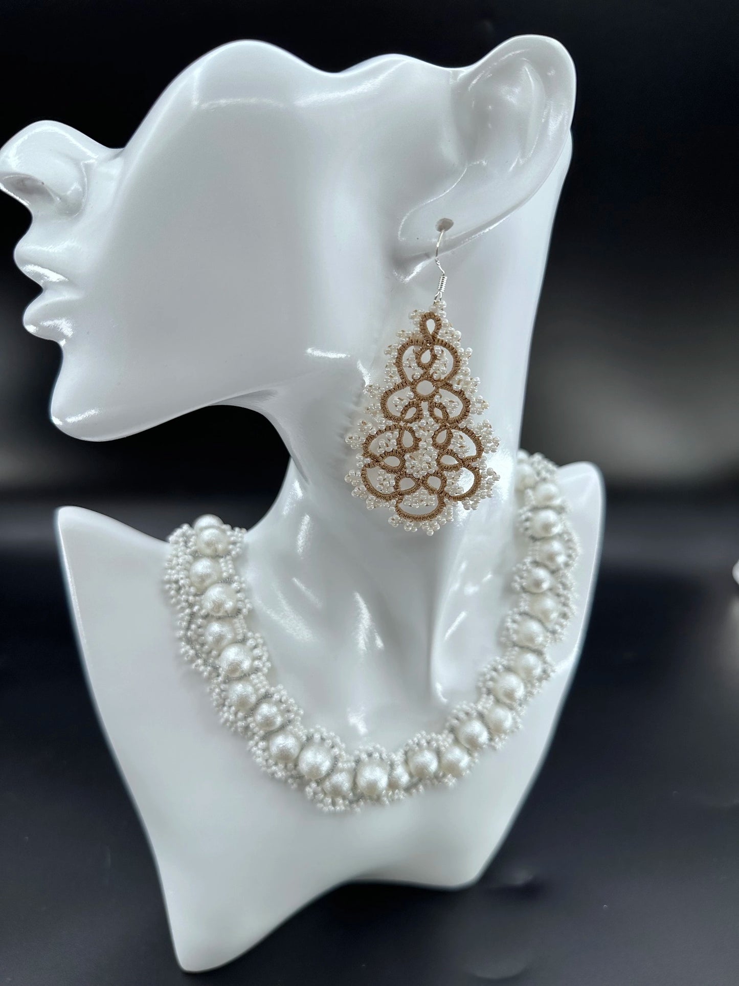 Close-up of a handmade Gourdlet dangle earring with intricate threadwork in khaki (earth yellow) and white glass beads, resembling a pear or gourd shape