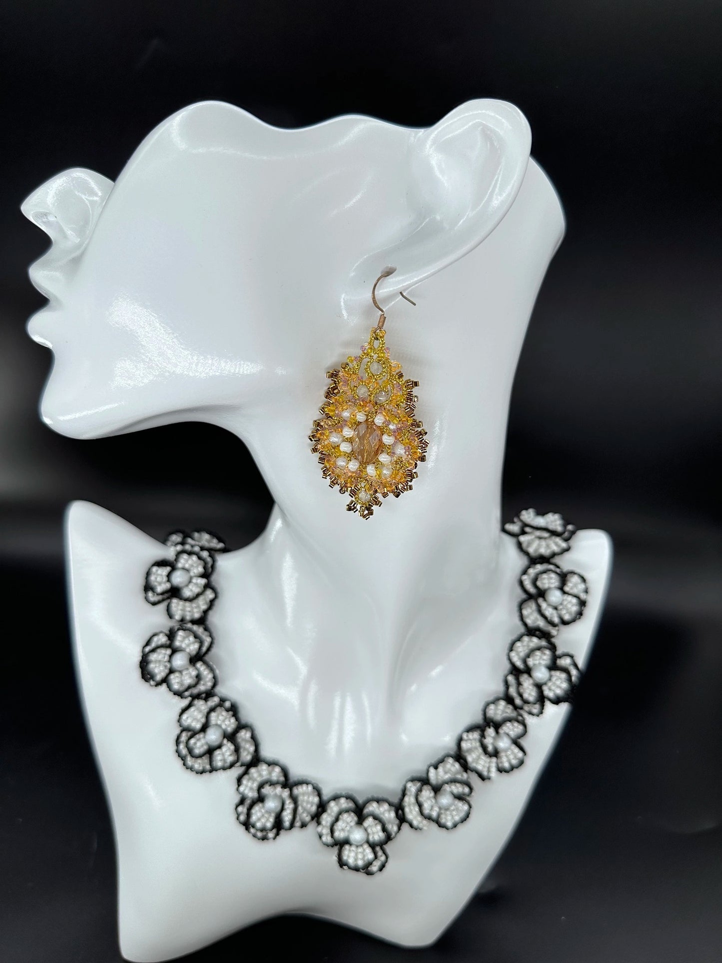 Close-up of a handcrafted Corelight dangle earring in rich amber, showcasing intricate gold threadwork and radiant clustered glass beads, made with unique **tatting** technique in an oval shape