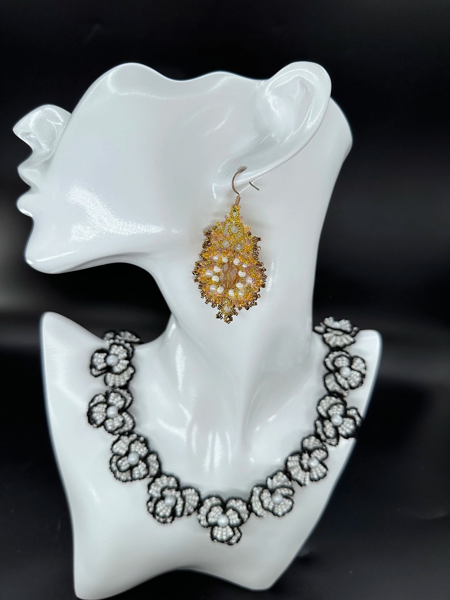 Close-up of a handcrafted Corelight dangle earring in rich amber, showcasing intricate gold threadwork and radiant clustered glass beads, made with unique **tatting** technique in an oval shape