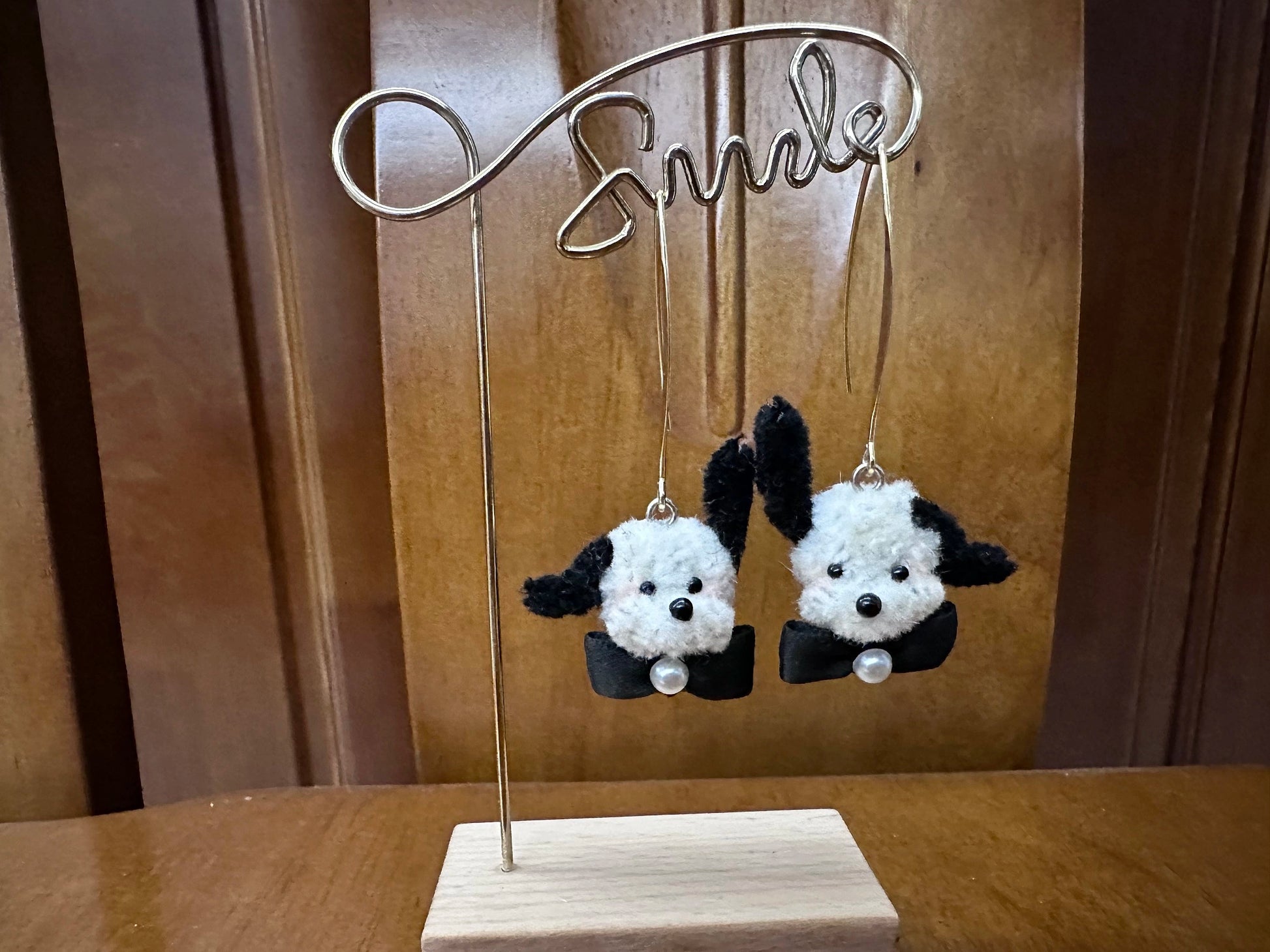 Handmade black and white wool twisted stick puppy head earrings with one floppy and one upright ear, featuring a small bow tie