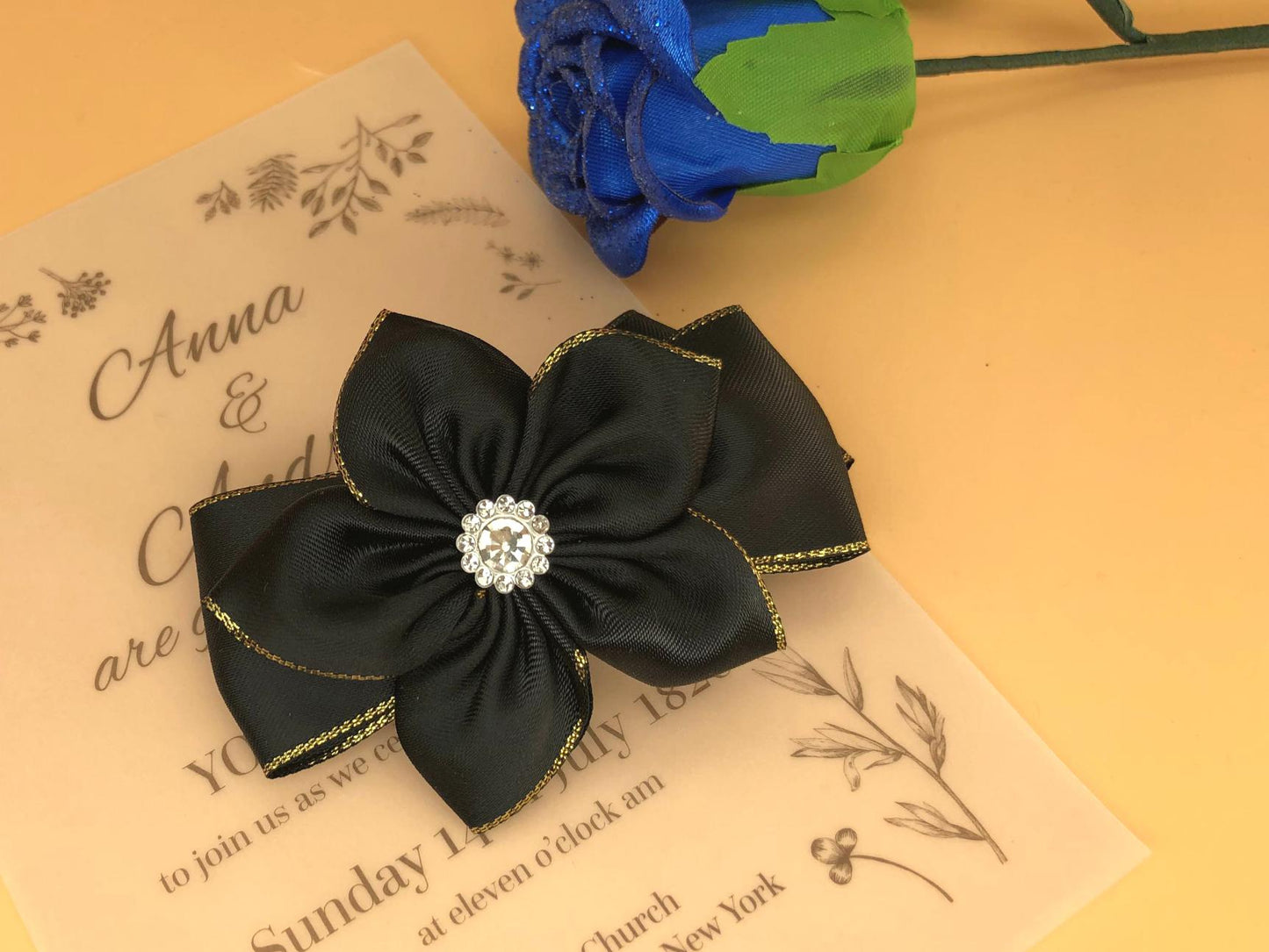 Handmade black satin ribbon hair clip featuring a layered flower with a sparkling rhinestone center, on a ribbon base.